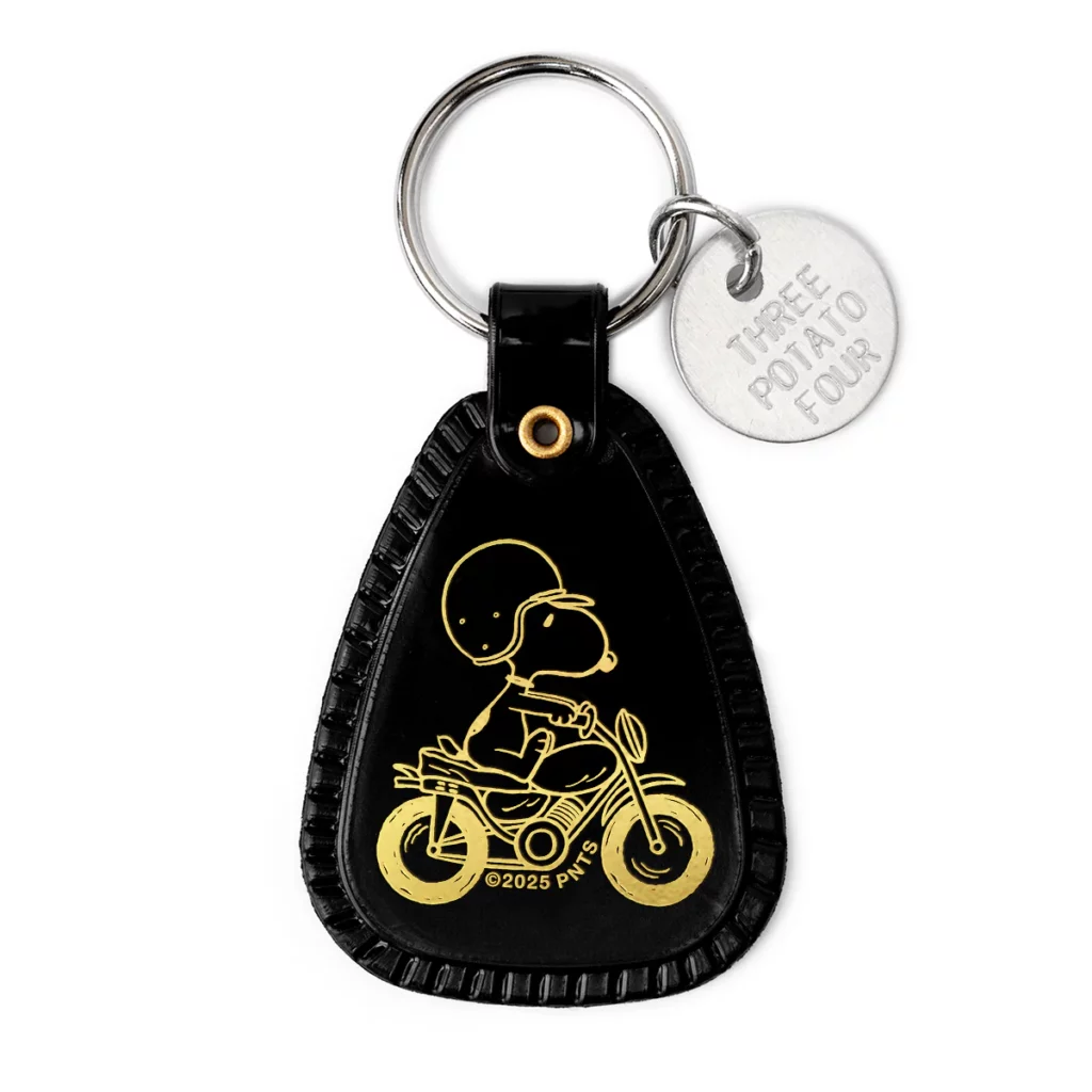 Vue du porte-clés “Snoopy Moto” : plastique semi-souple, impression Snoopy sur fond style vintage motel-tag, dimensions ~3,8×5,7 cm, anneau clé en acier, idéal pour clés ou sac.